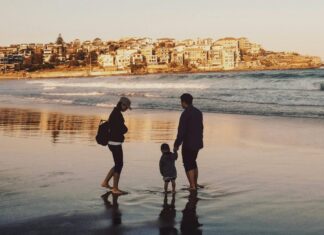 How to Save Money on a Family Vacation Man and Woman Walking With Boy in Seashore