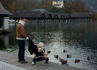 Best Travel Strollers For Your Little Ones Father with child in stroller standing on embankment of lake