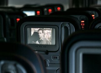 3 Films That Are Perfect For Long-Haul Flights A plane's interior, with empty seats and a movie on a screen.