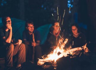 Best Cooking Gear to Take on Camping Trips Friends sitting around the campfire at nightimes