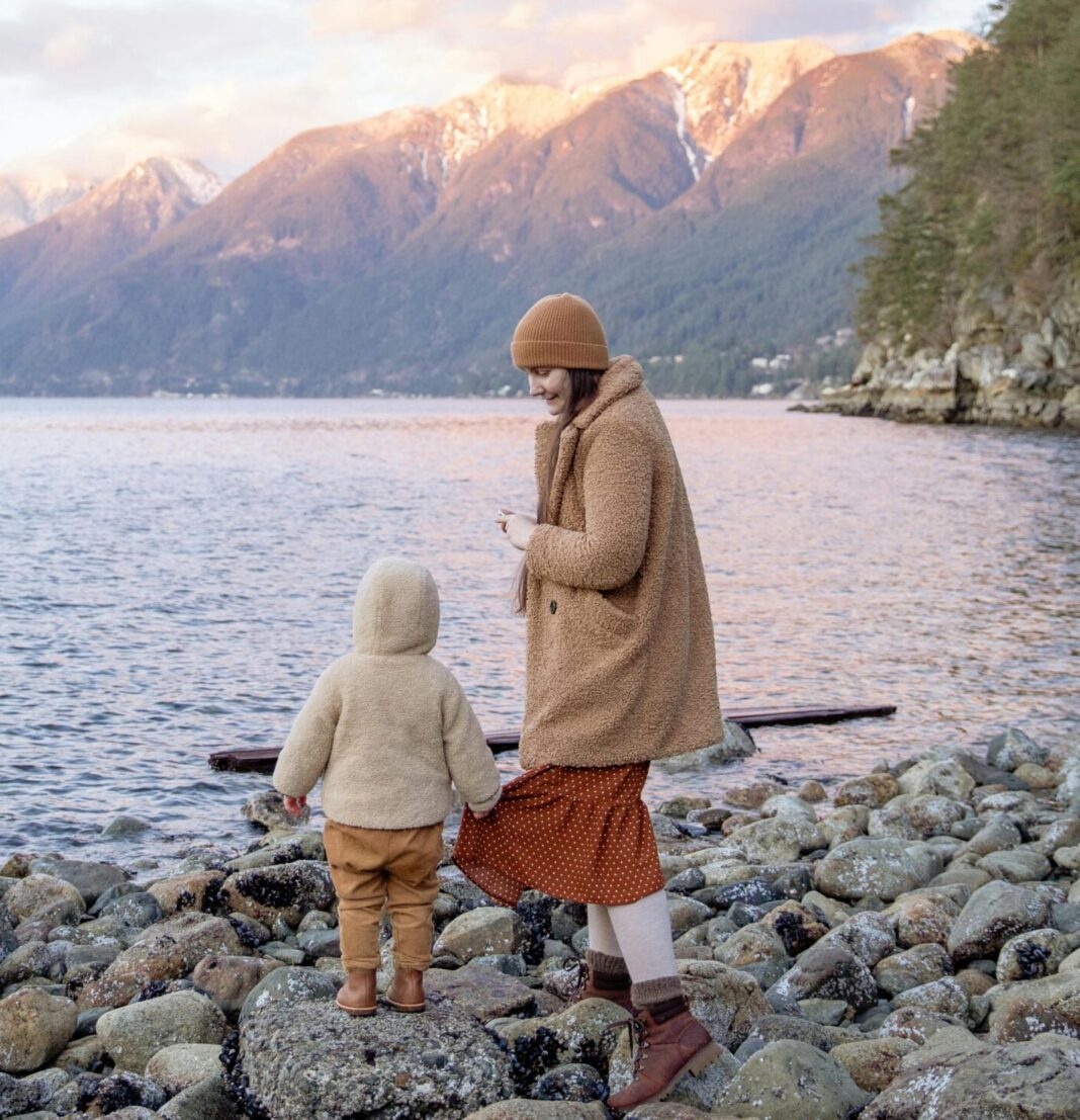 Mother and faceless little child on rocky shore near lake and mountains