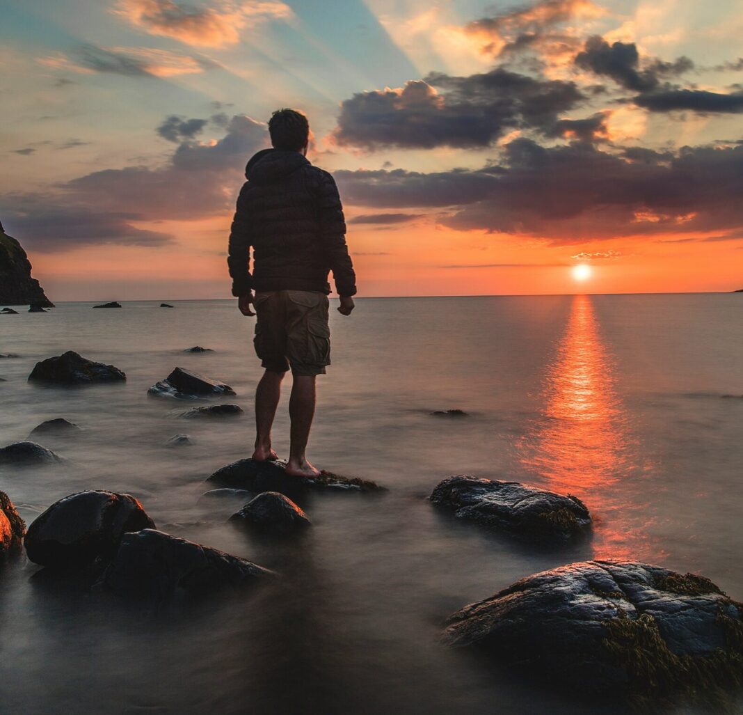 Man standing on a rocky shore during sunset