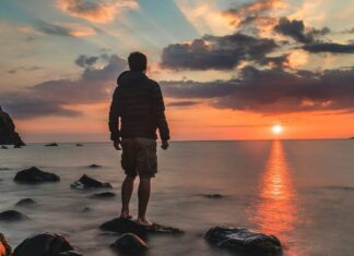 Here are Some of the Best Beaches in Scotland Man standing on a rocky shore during sunset