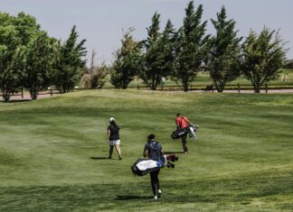 Iconic Travel Destinations For Golf Lovers People Walking on Green Grass Field Carrying Golf Bags